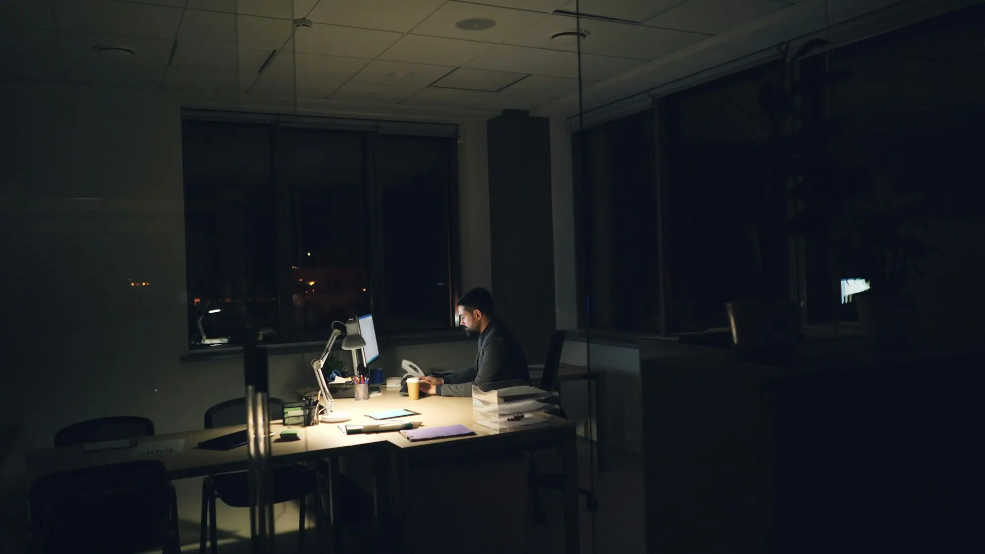 Business owner thinking at a desk lit by a lamp at midnight